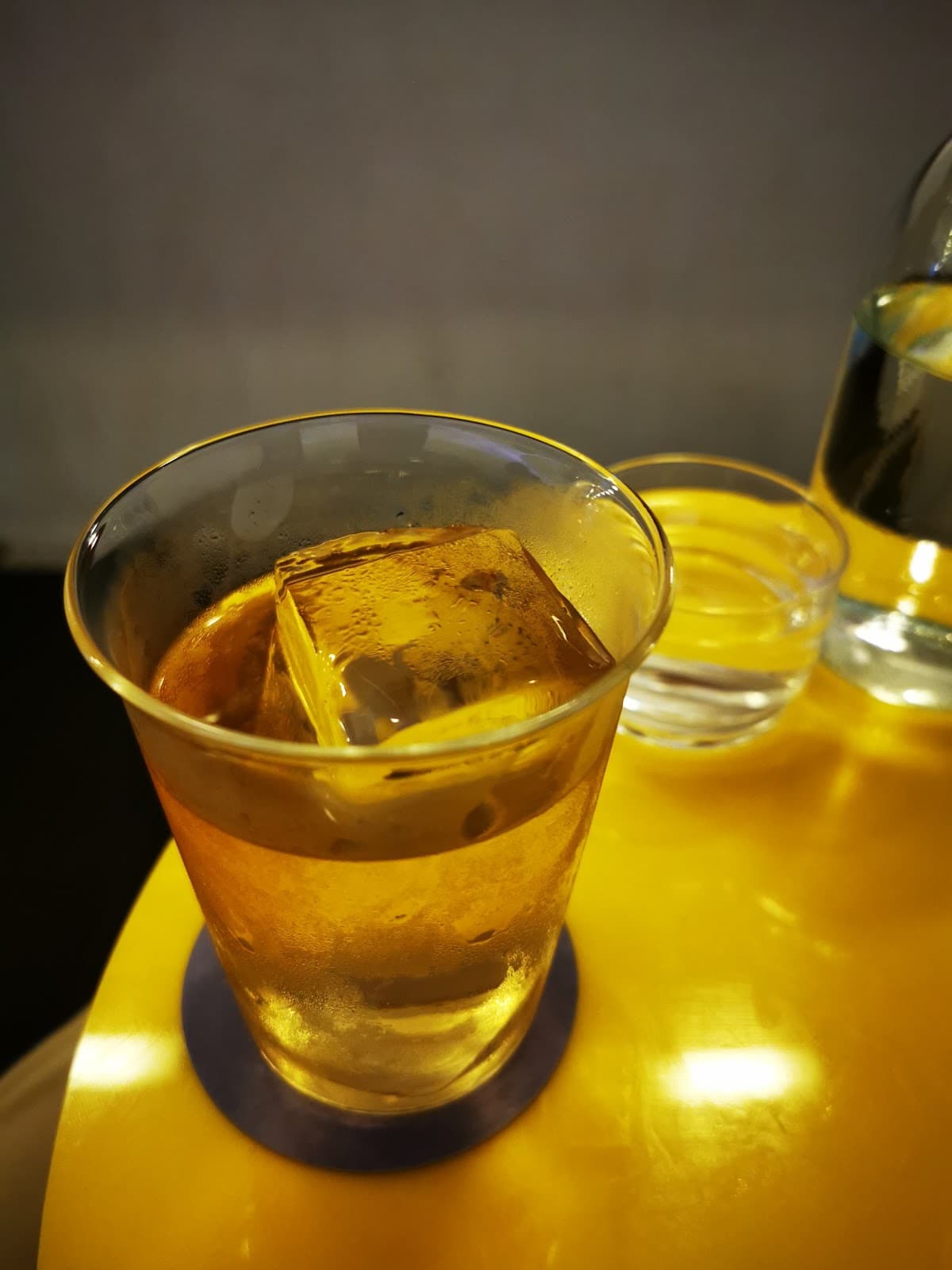 Glass with large ice cube on a yellow table in London