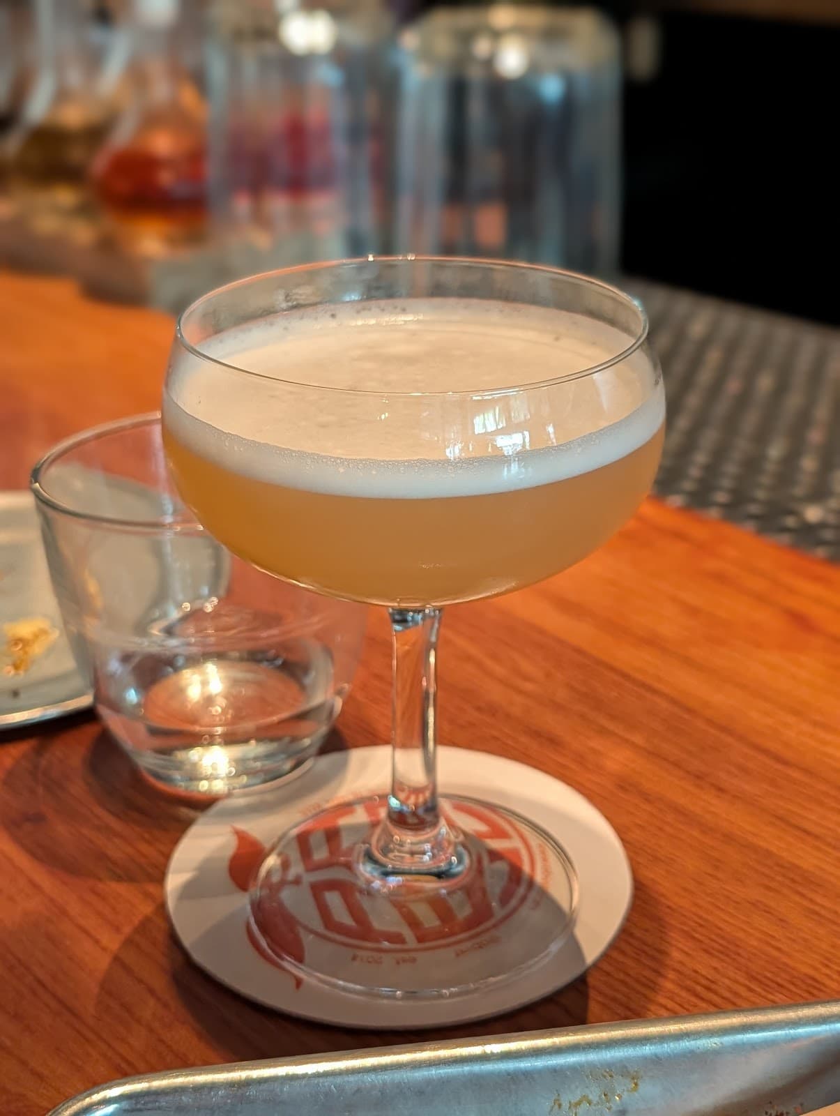 Close-up of a cocktail in a coupe glass on a bar with a glass and plate nearby in San Francisco