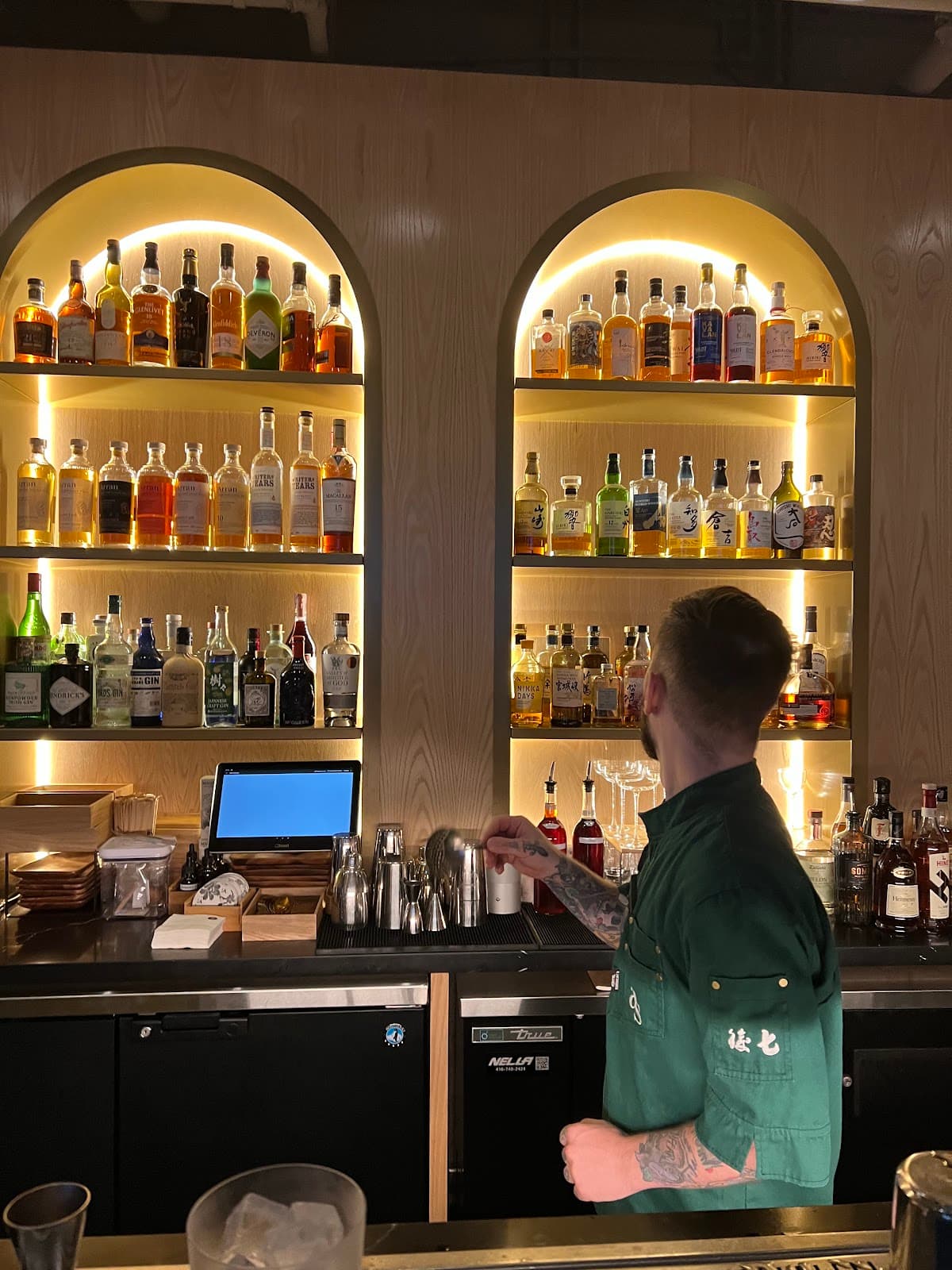 Bartender at illuminated bar shelves with various liquor bottles in Toronto