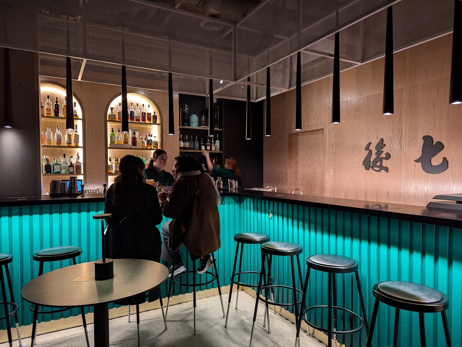 Stylish bar interior with teal bar counter and patrons enjoying drinks in Toronto