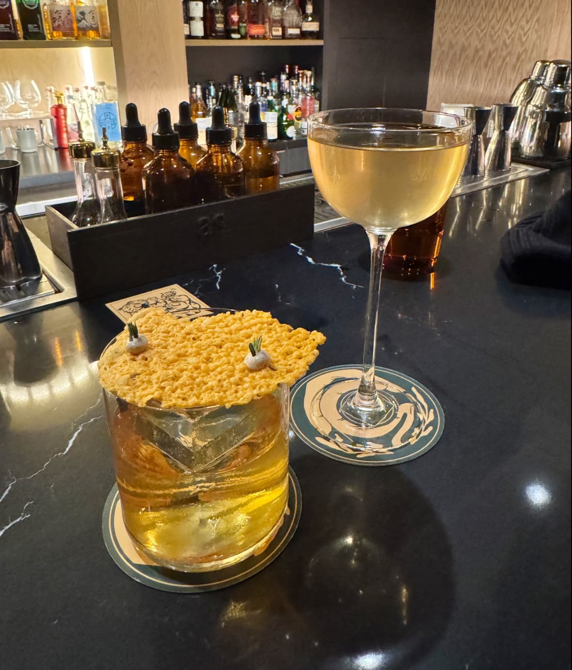 Close-up of two cocktails on a bar counter with bottles in the background in Toronto