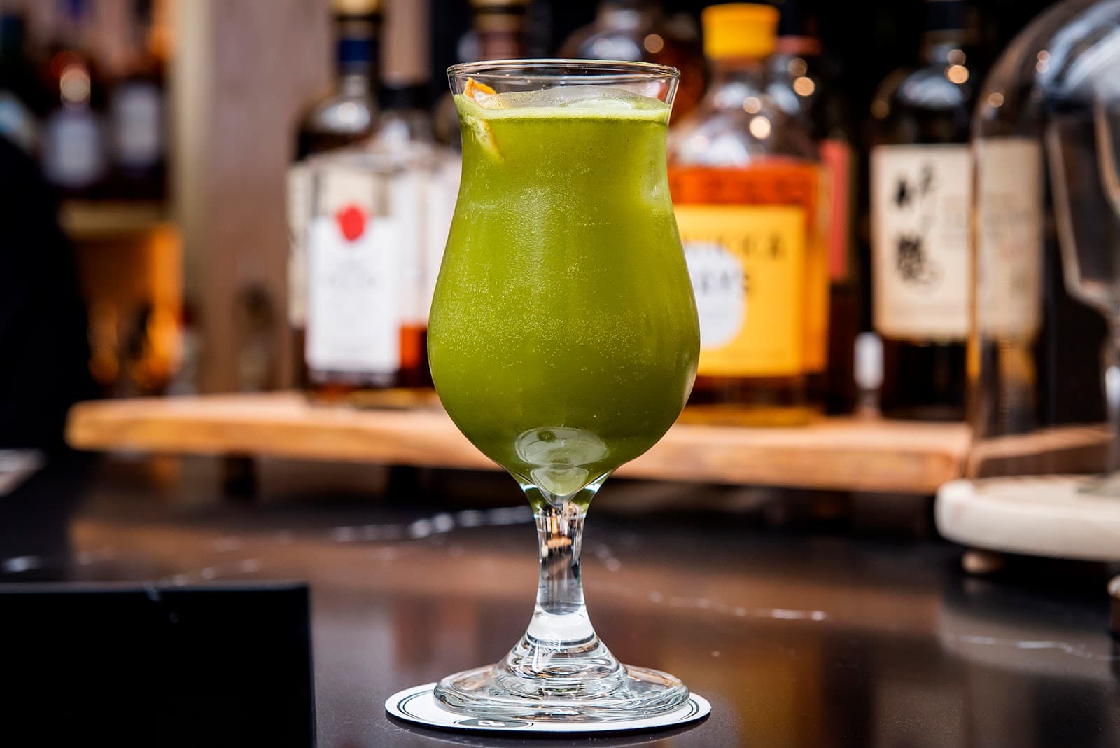Green cocktail in a glass with bottles blurred in the background in Toronto
