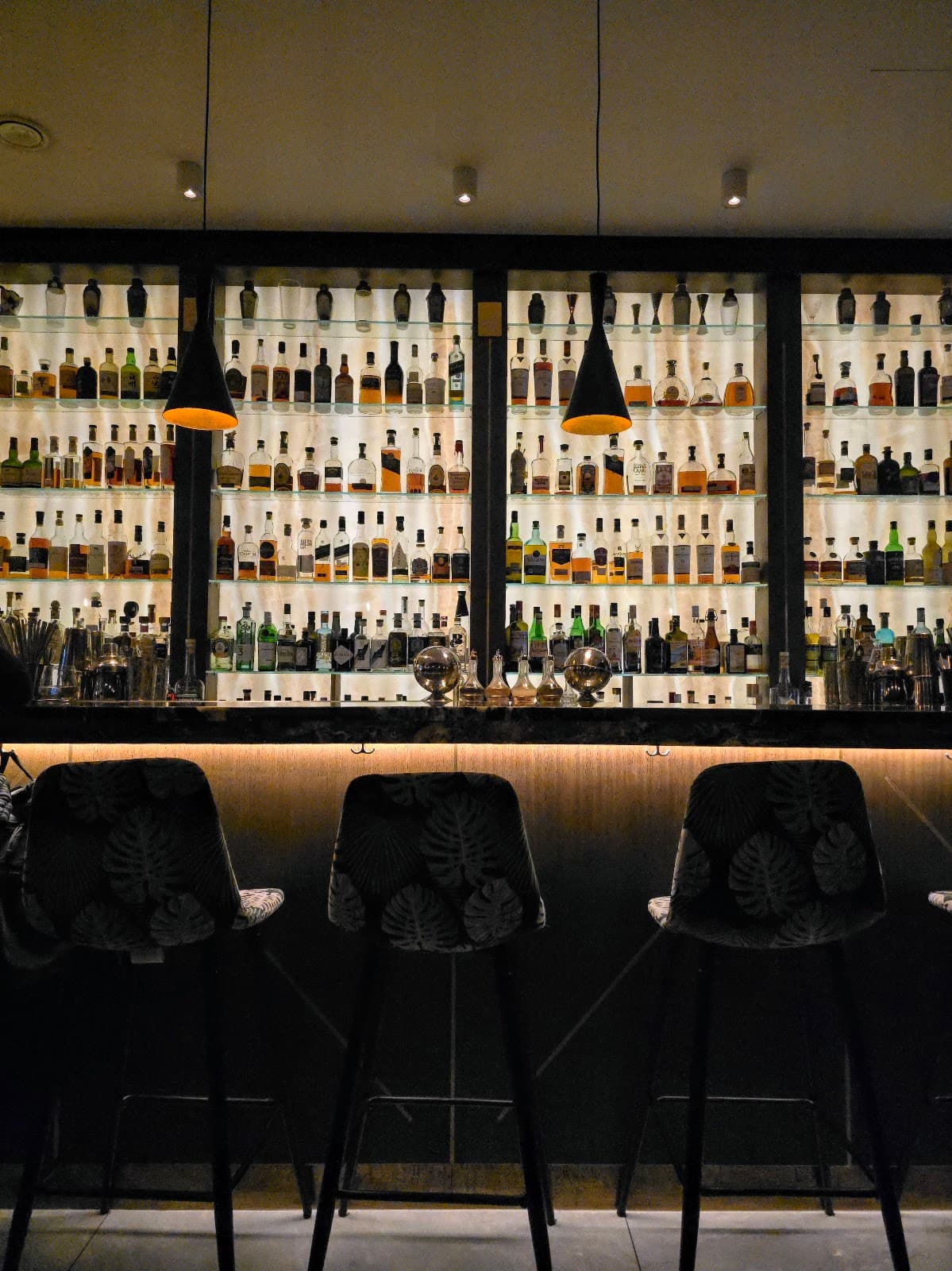Elegant bar with backlit shelves filled with bottles and stylish bar stools in London