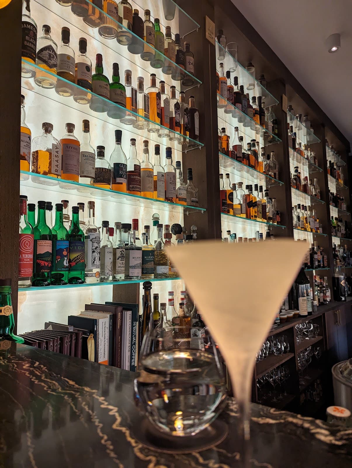 Bar counter with a variety of liquor bottles on illuminated shelves in London