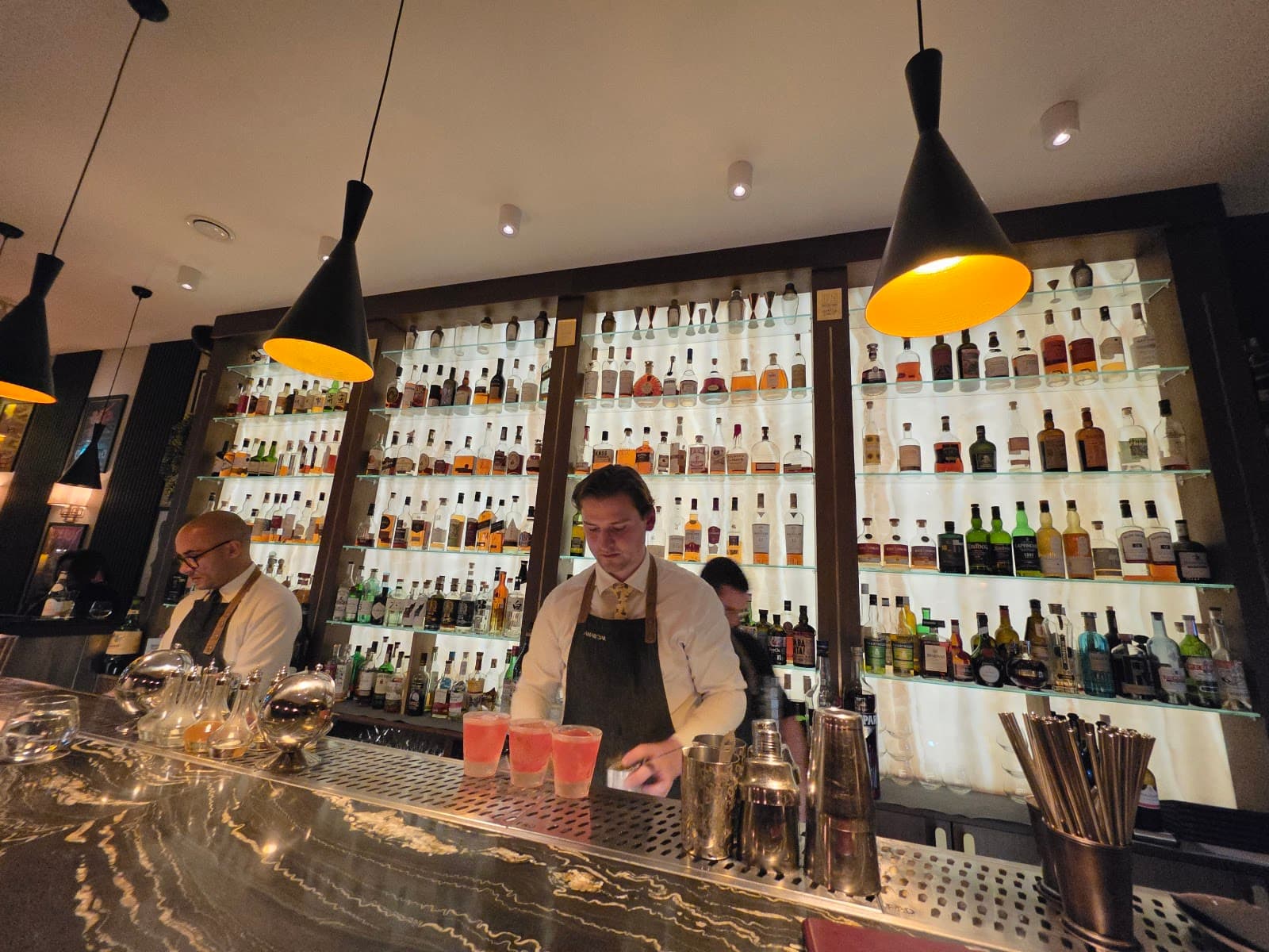Professional bartenders behind a well-stocked bar with hanging lights in London