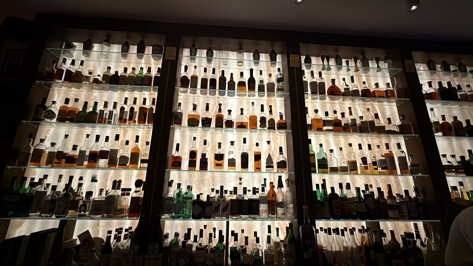 Backlit bar shelves with various liquor bottles on display in London