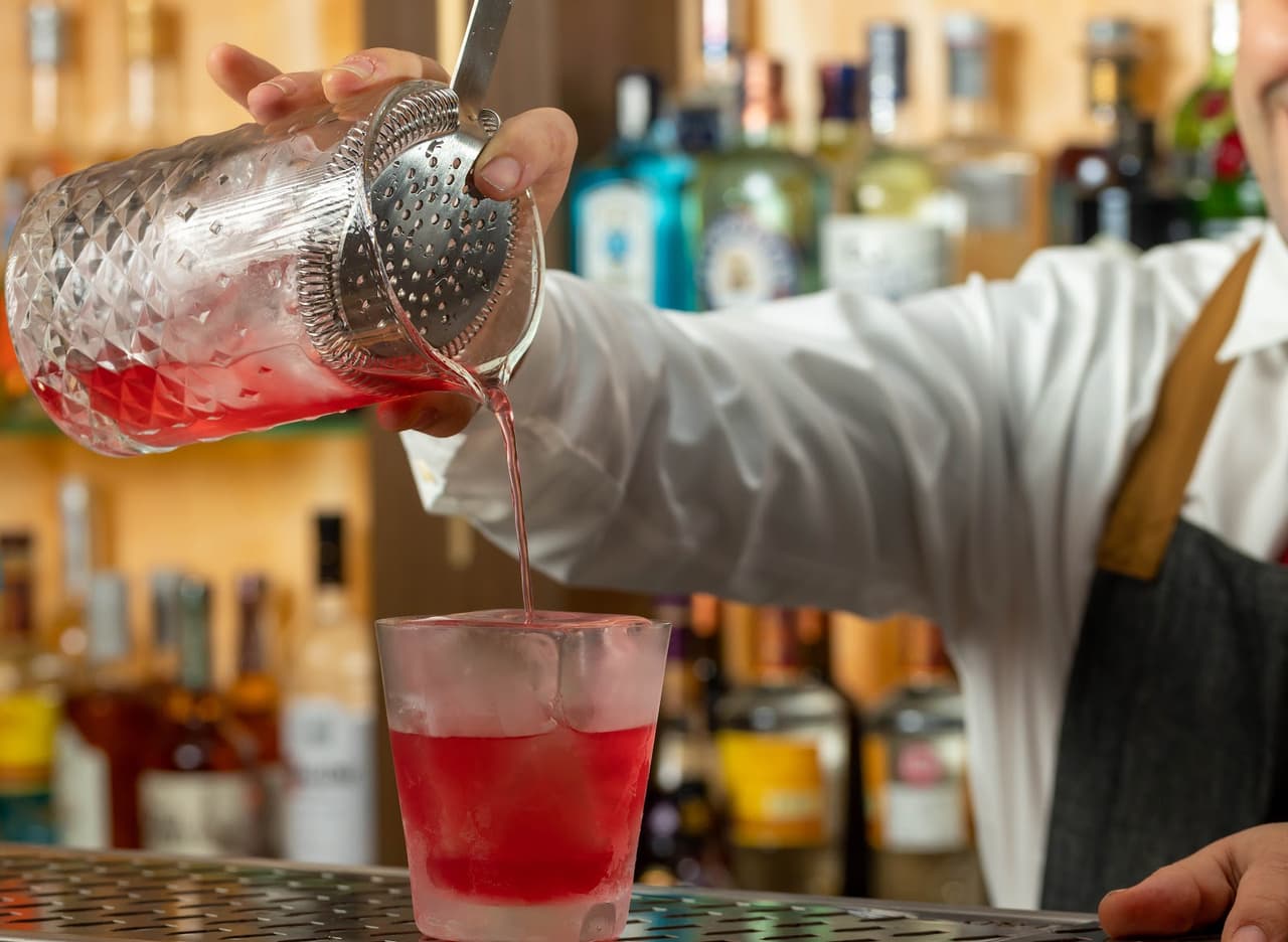 Bartender pouring red cocktail from shaker into glass at bar in London