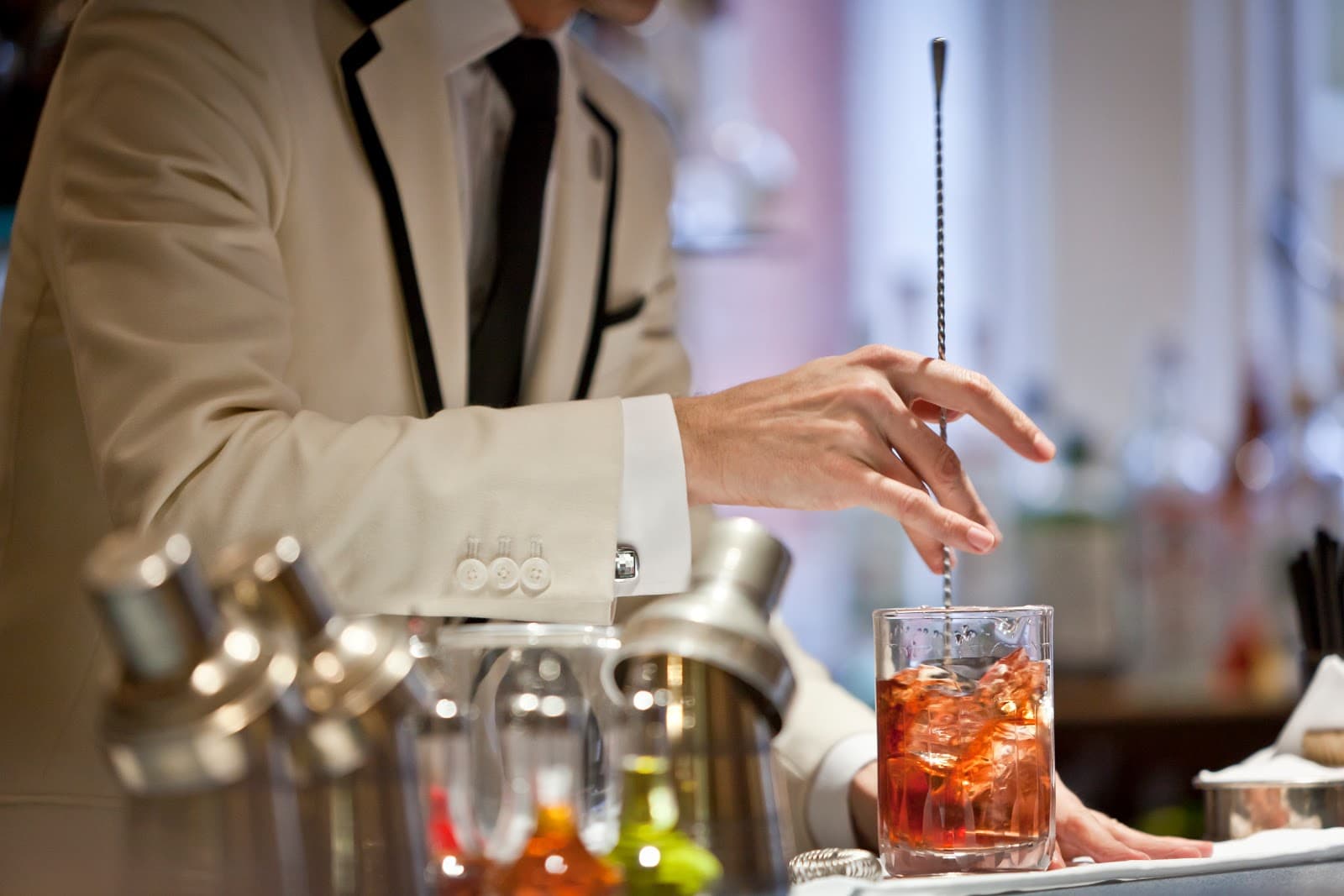 Bartender in white jacket stirring a cocktail with a long spoon in London
