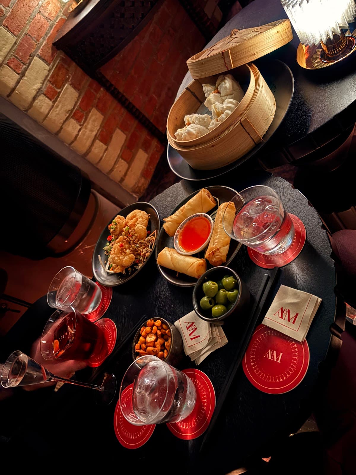 Cocktail bar table with drinks and dim sum against a brick wall at Avi bar in London