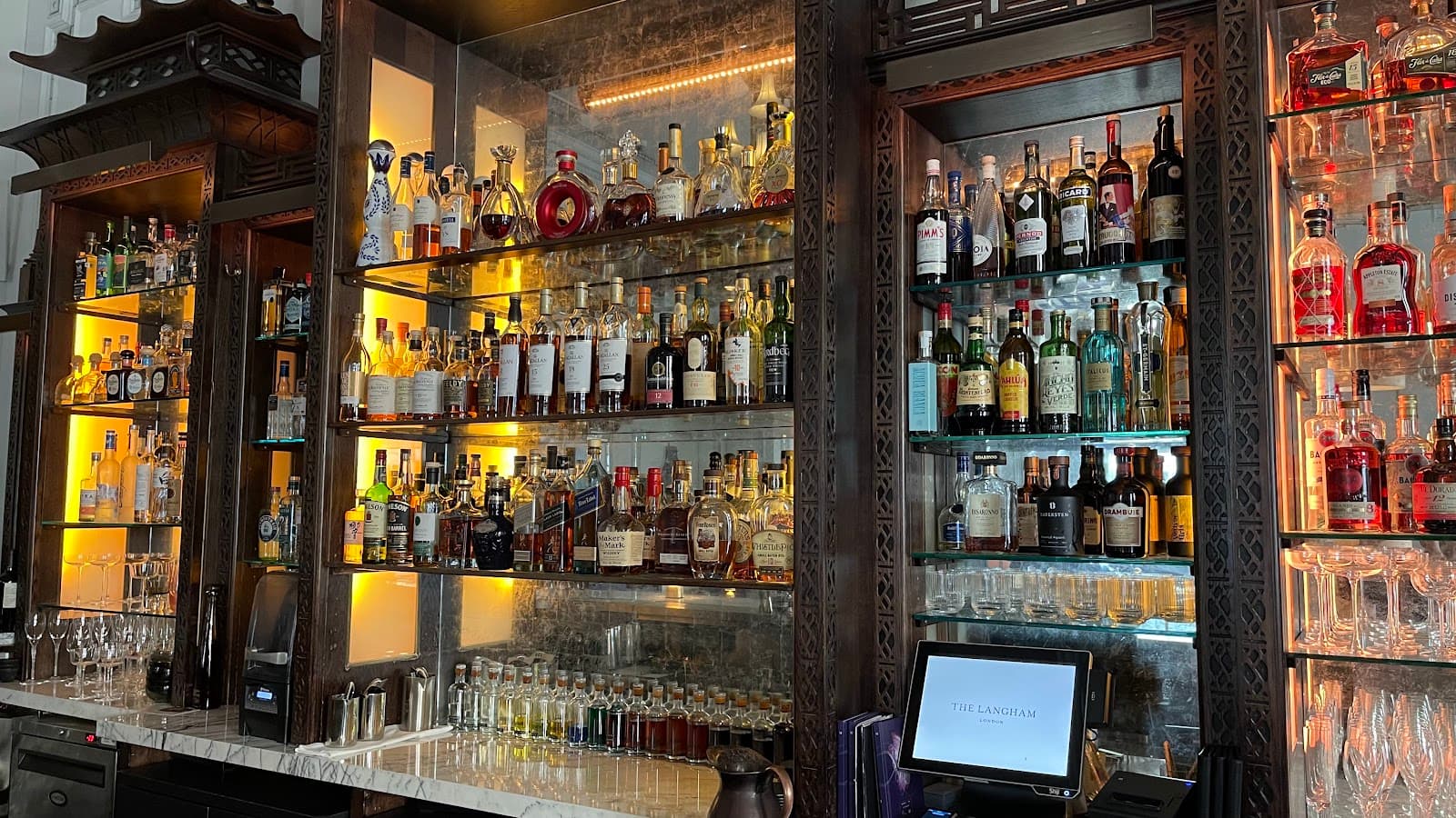 Elegant bar with illuminated liquor shelves and marble counter at The Langham in London