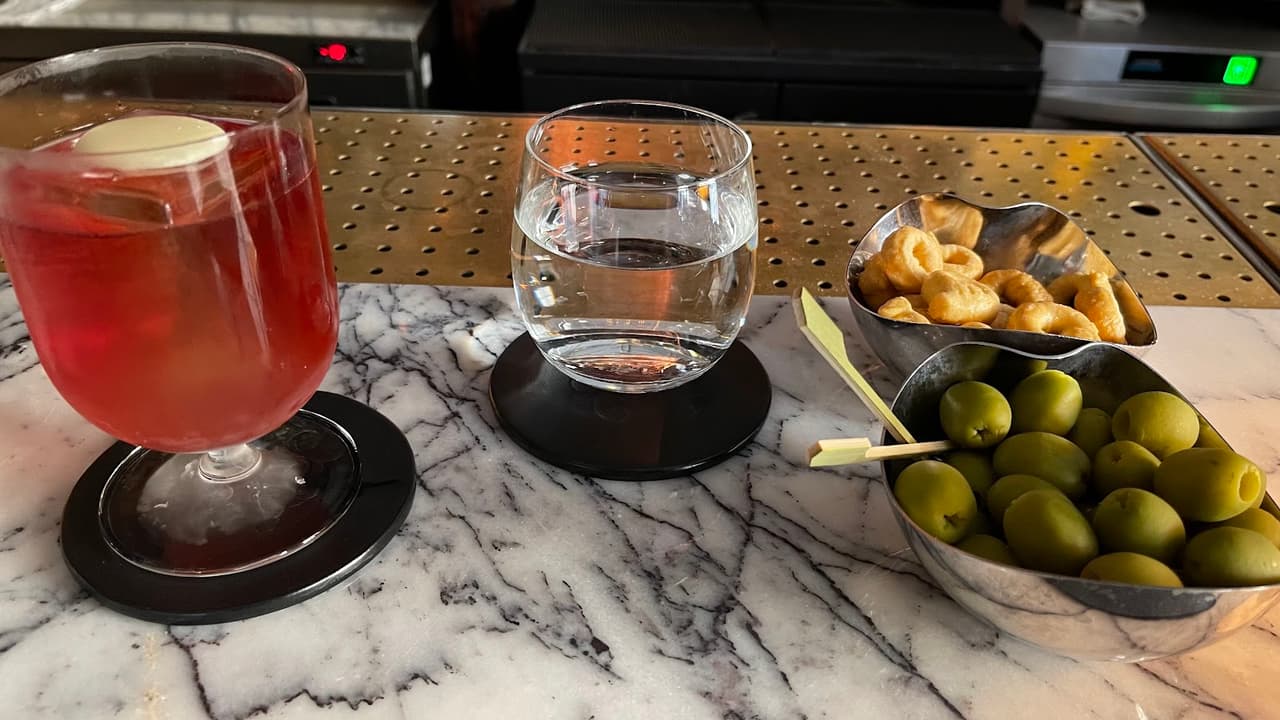 Cocktail glass with red drink, water glass, and snacks on a marble bar counter in London