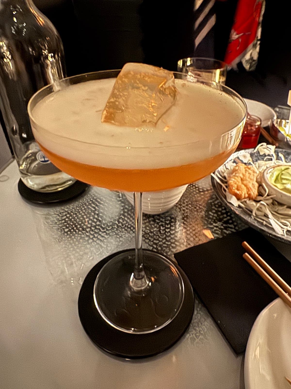 Cocktail glass with large ice cube on a table with plates and chopsticks in London