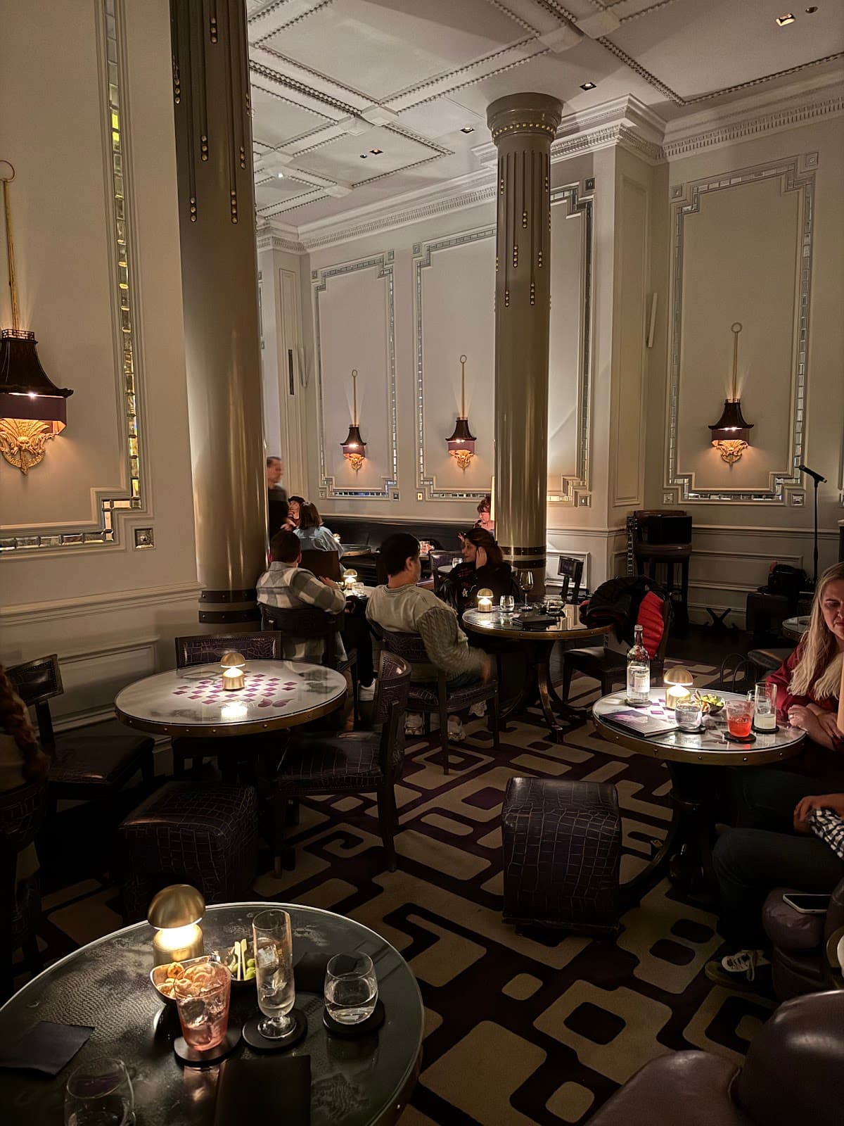 Elegant interior with columns, cozy lighting, and patrons at small tables in London