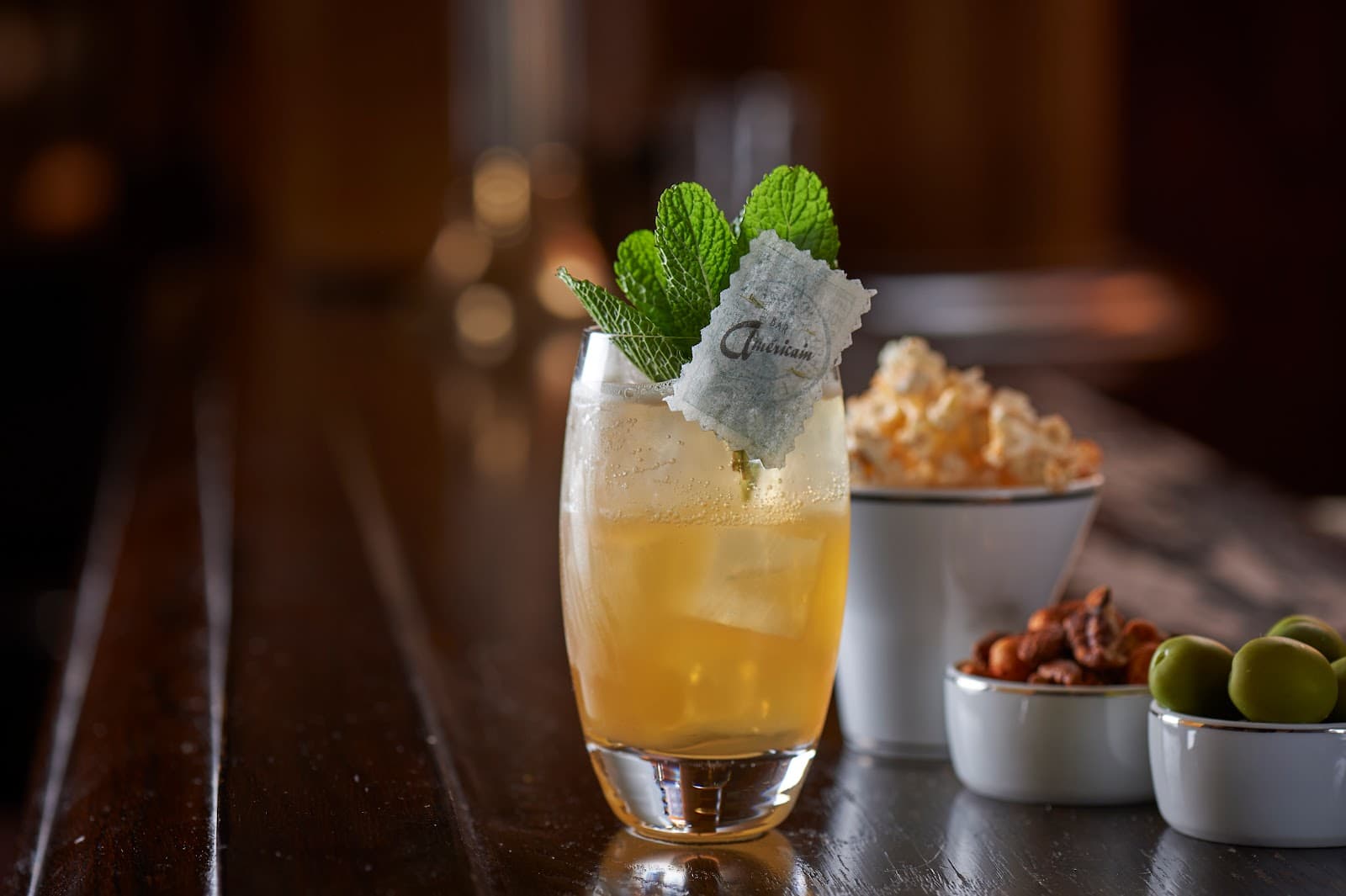 Close-up of a cocktail with mint and snacks on a wooden bar counter in London