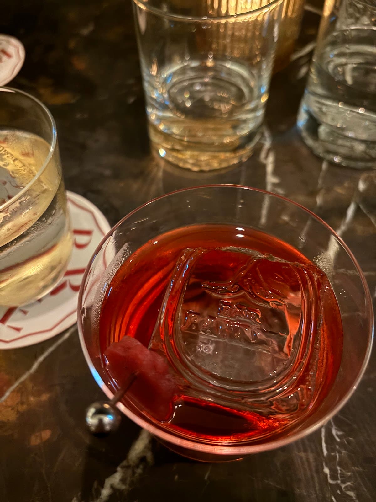 Close-up of a cocktail with a large ice cube on a dark marble bar counter in Toronto