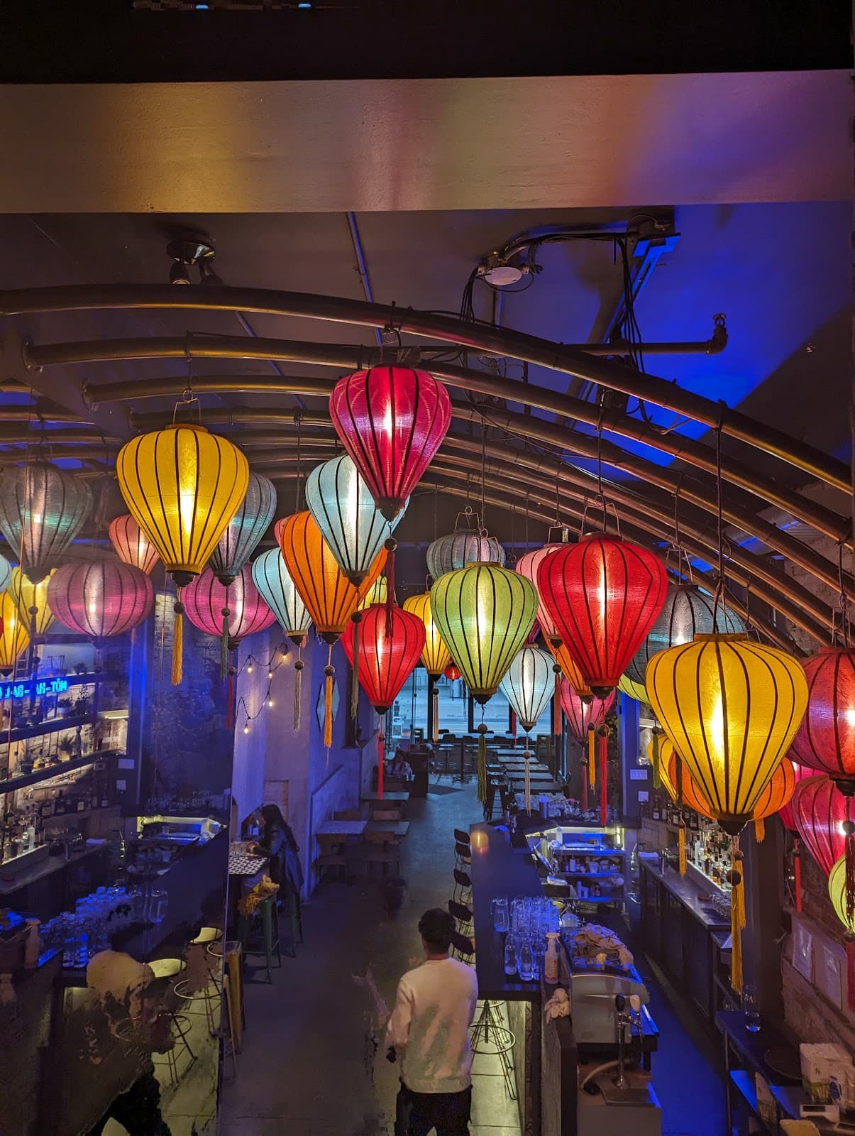 Colorful lanterns hanging over a dimly lit bar with tables and chairs