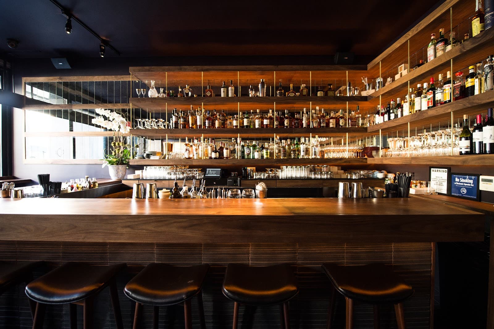 Well-stocked bar with wooden shelves and stools in a dim setting