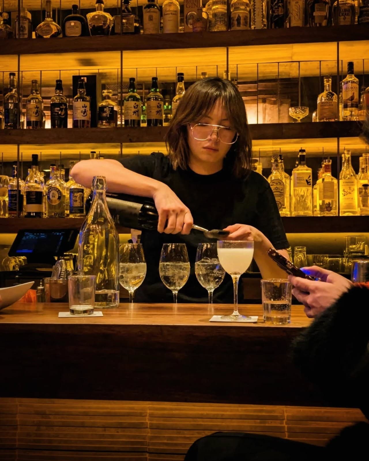 Bartender pouring drinks at a well-stocked bar with illuminated shelves in New York