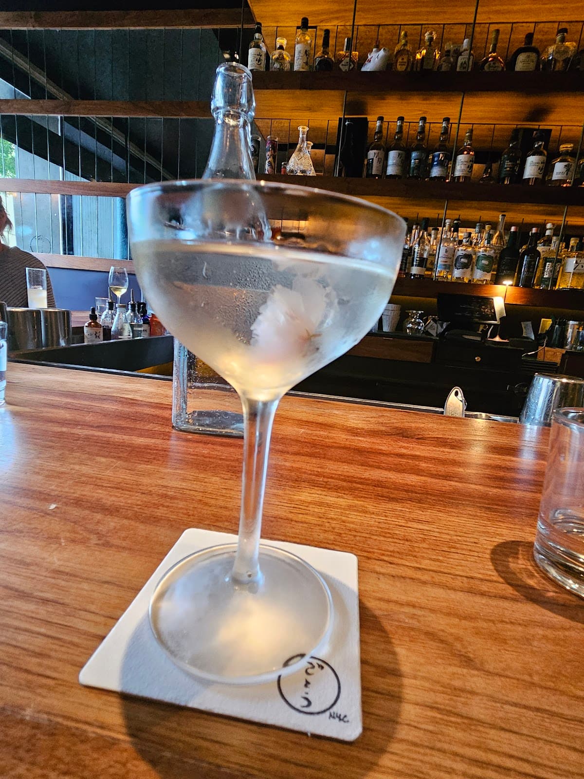 Cocktail glass on a wooden bar counter with shelves of bottles in background in New York