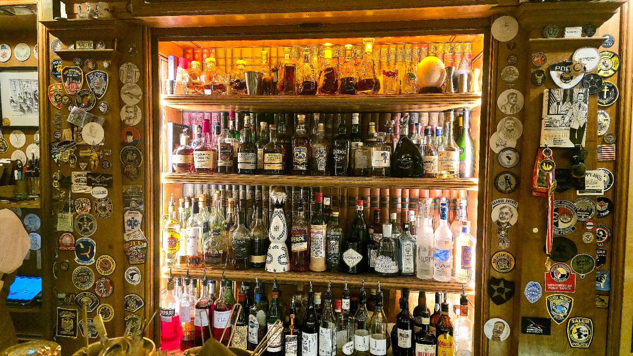 Illuminated bar shelves with various liquor bottles and decorative patches in Paris