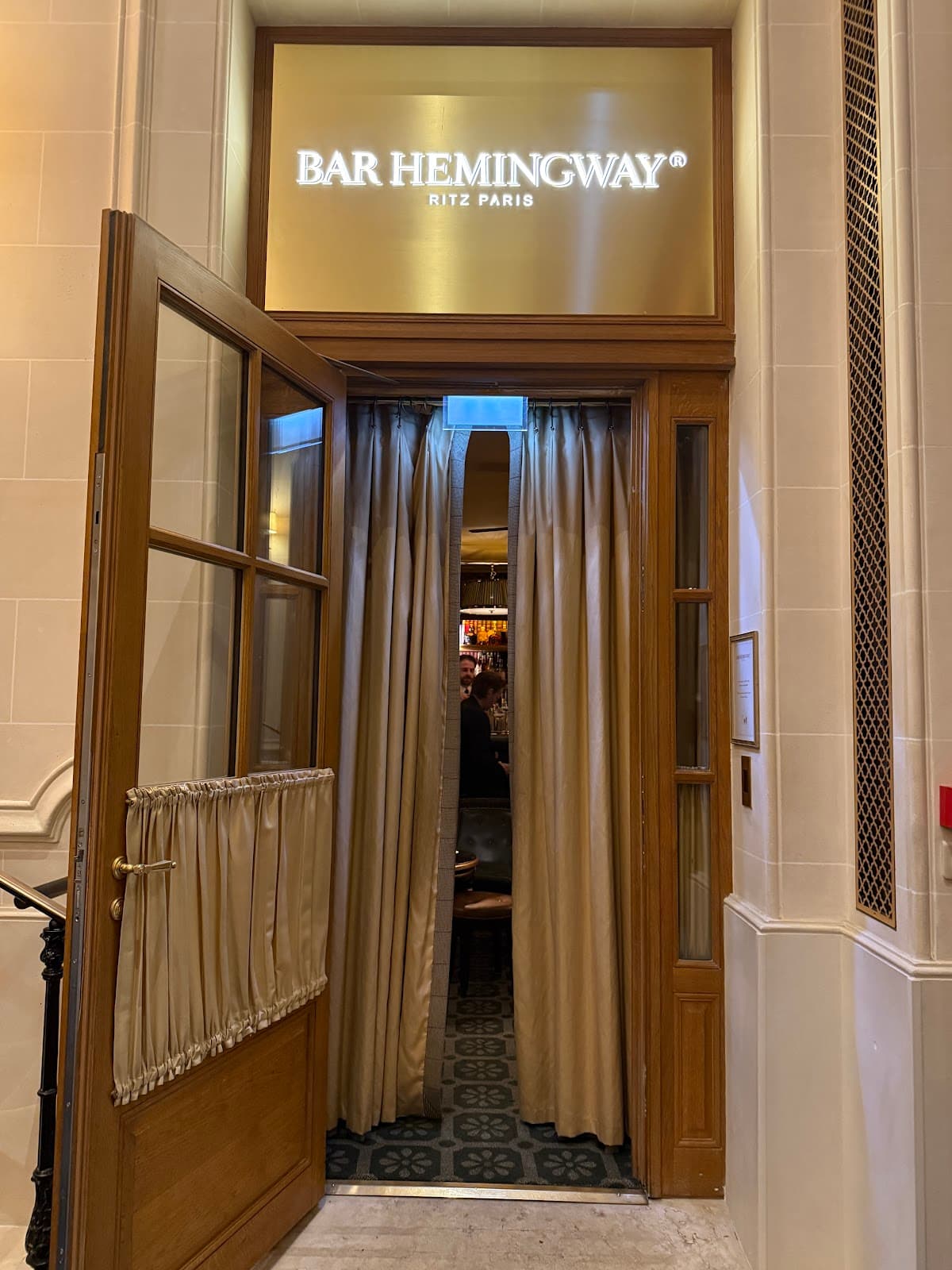 Entrance to Bar Hemingway at Ritz Paris with open wooden doors and curtains in Paris