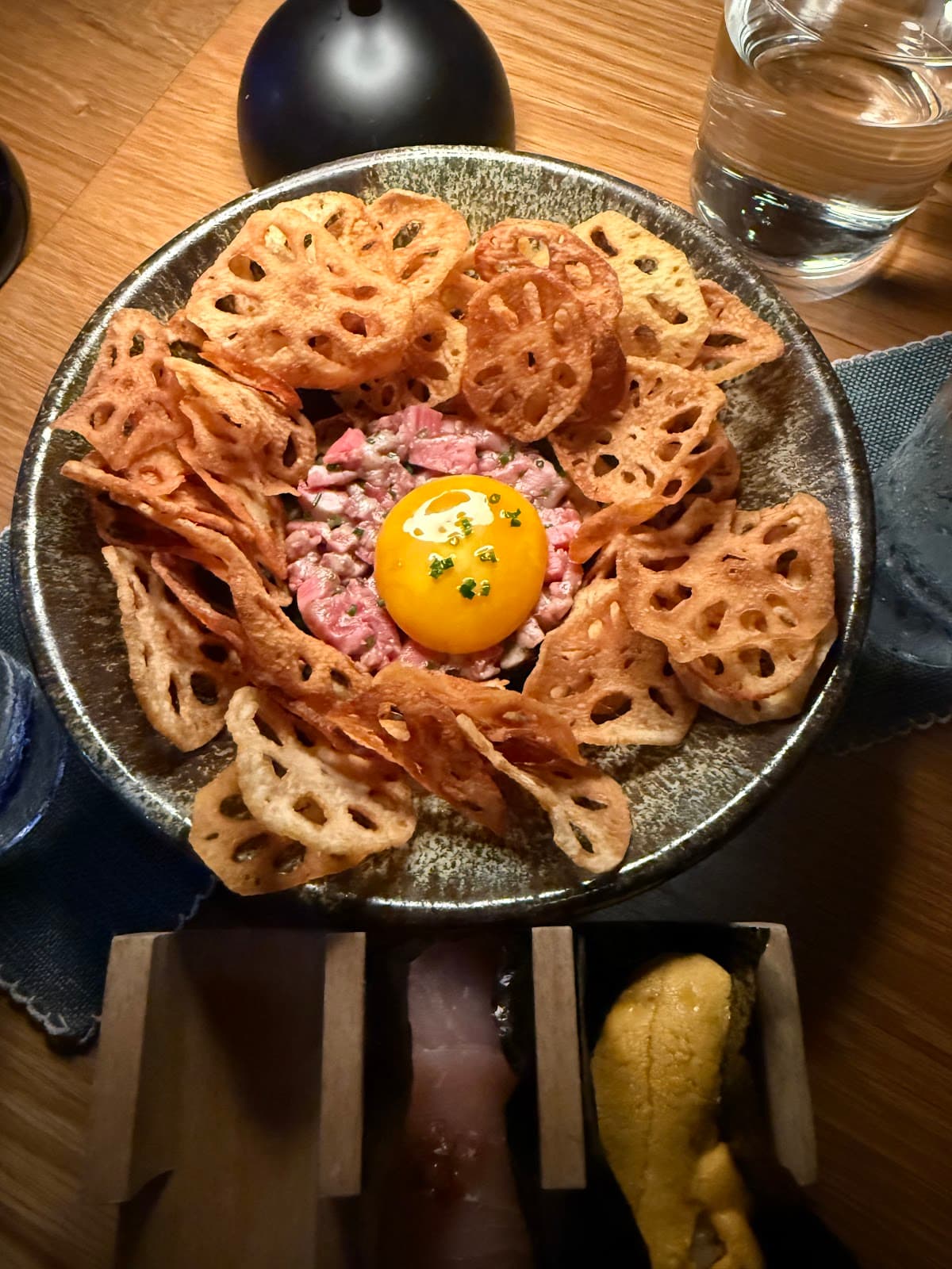 Plate with yolk and lotus root chips on wooden table at a cocktail bar in San Francisco