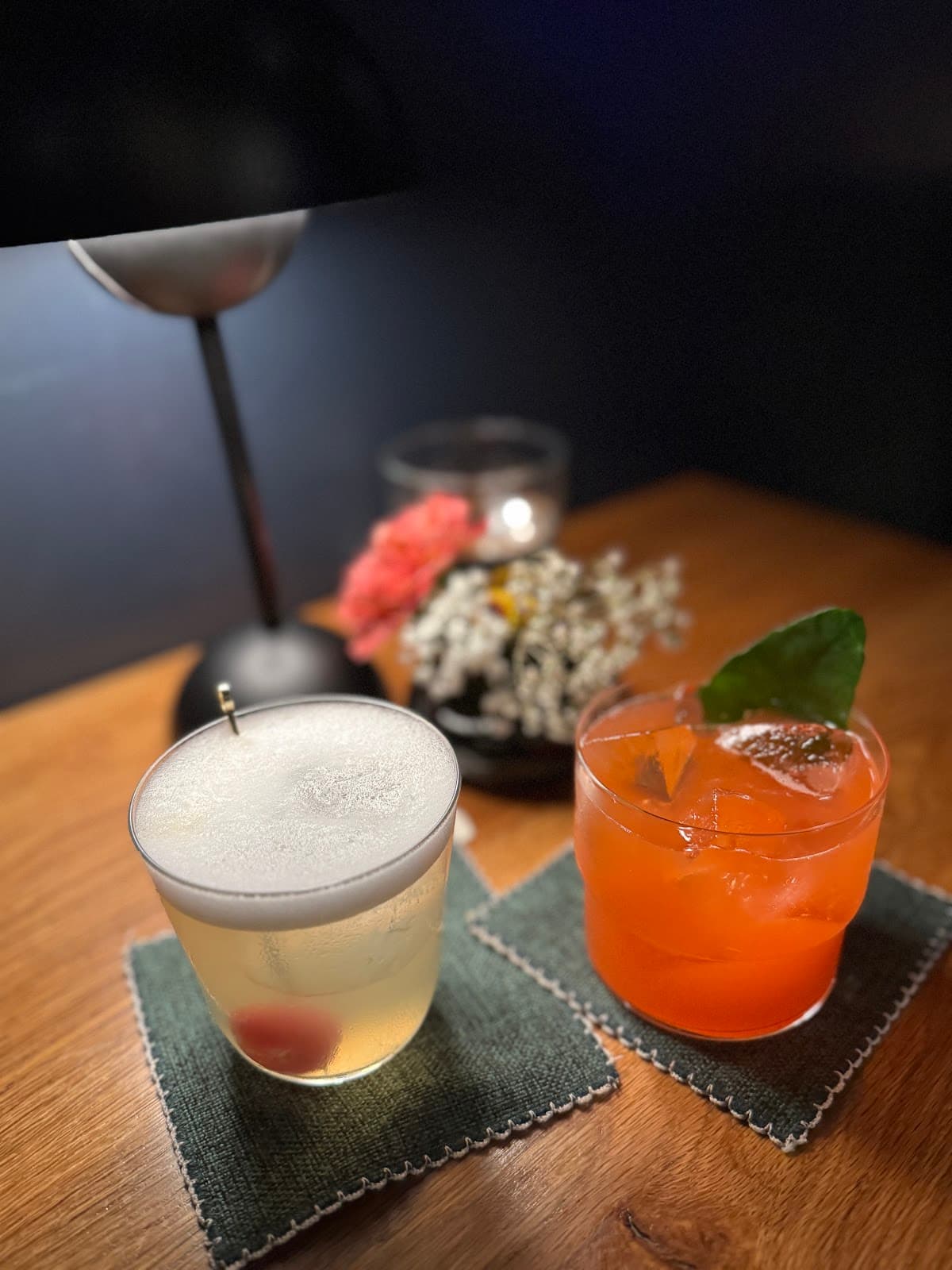 Two cocktails on a wooden table with a lamp and flowers in the background in San Francisco