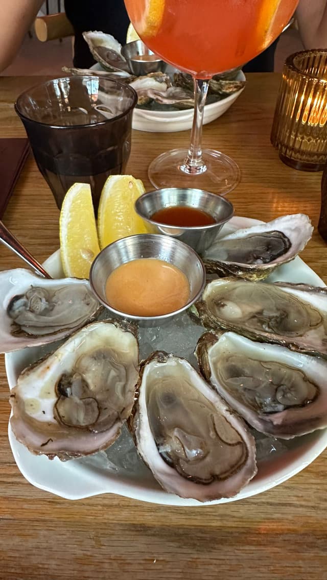 Plate of oysters with cocktail and lemon wedges on a wooden table in Toronto