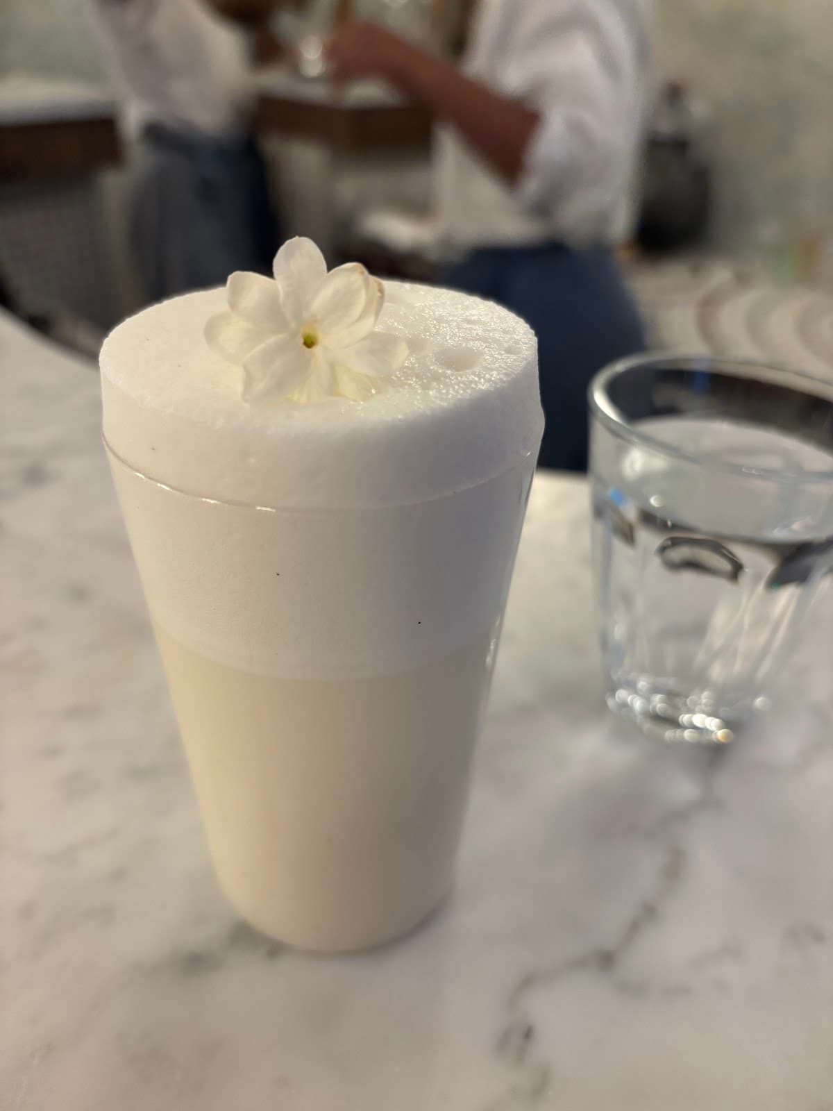 Cocktail with frothy top and flower garnish on marble table in Paris