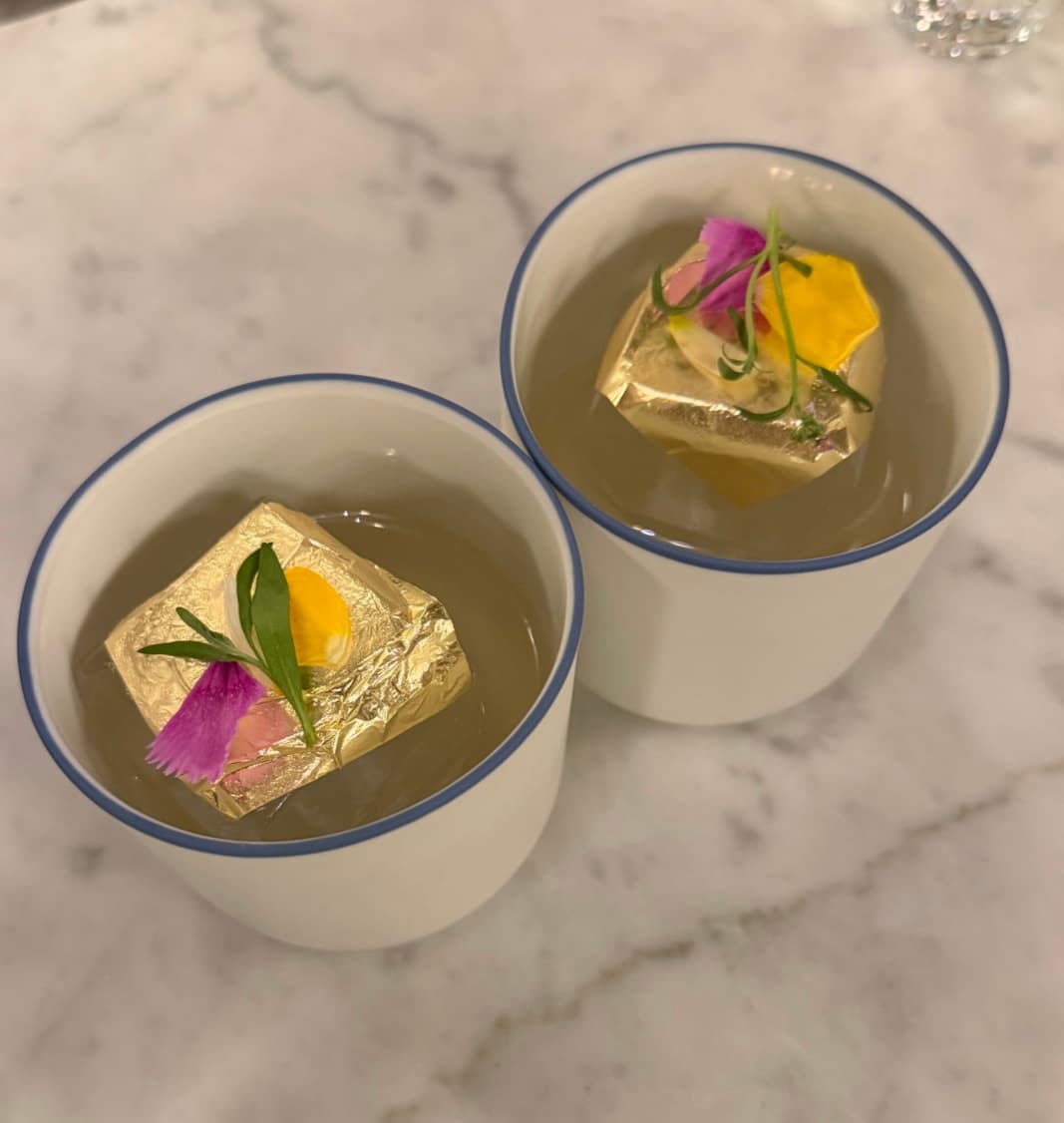 Two elegant cocktails with gold foil garnish and flowers on a marble surface in Paris