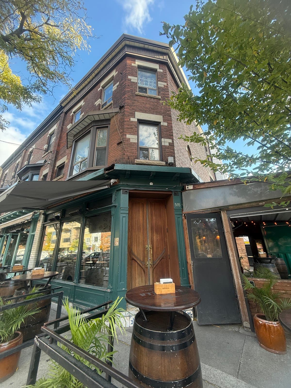 Brick exterior of corner building with wooden entrance and outdoor tables in Toronto