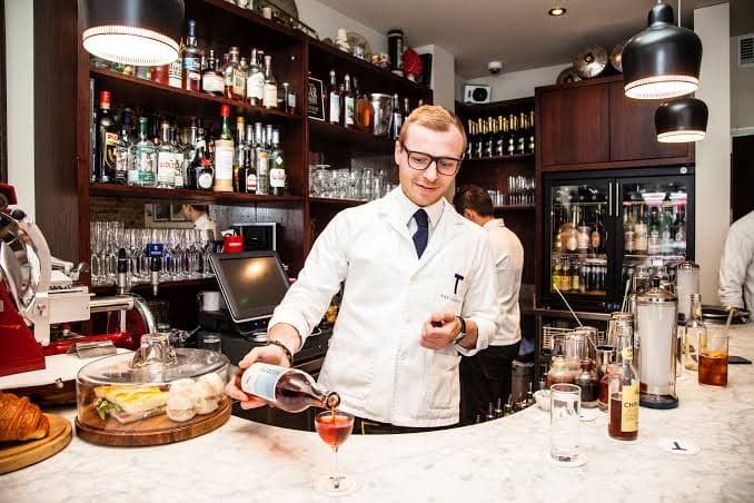 Bartender pouring a drink at a well-stocked bar with bottles in the background