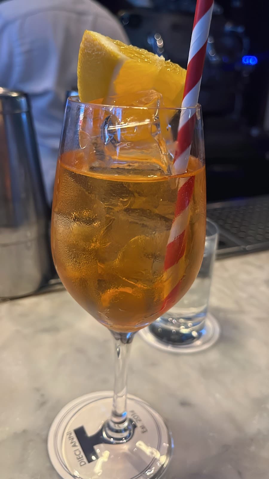 A cocktail in a glass with an orange slice and striped straw on a bar in London