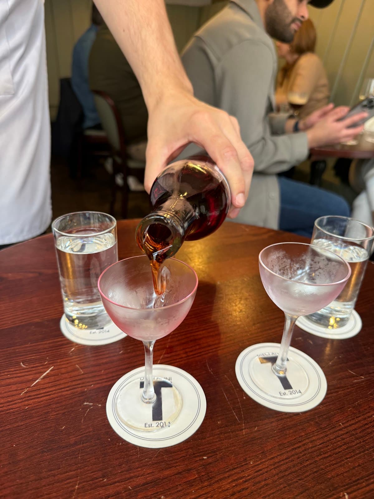 Bartender pouring drink into frosted glass on a wooden table in London