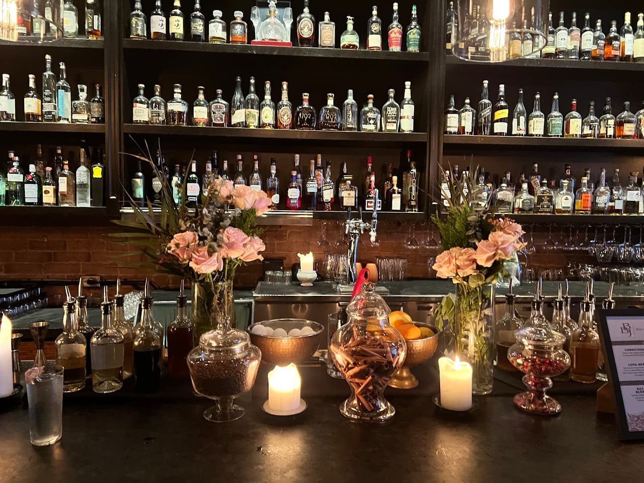 Bar counter with bottles, flowers, and candles in a cocktail bar in Toronto