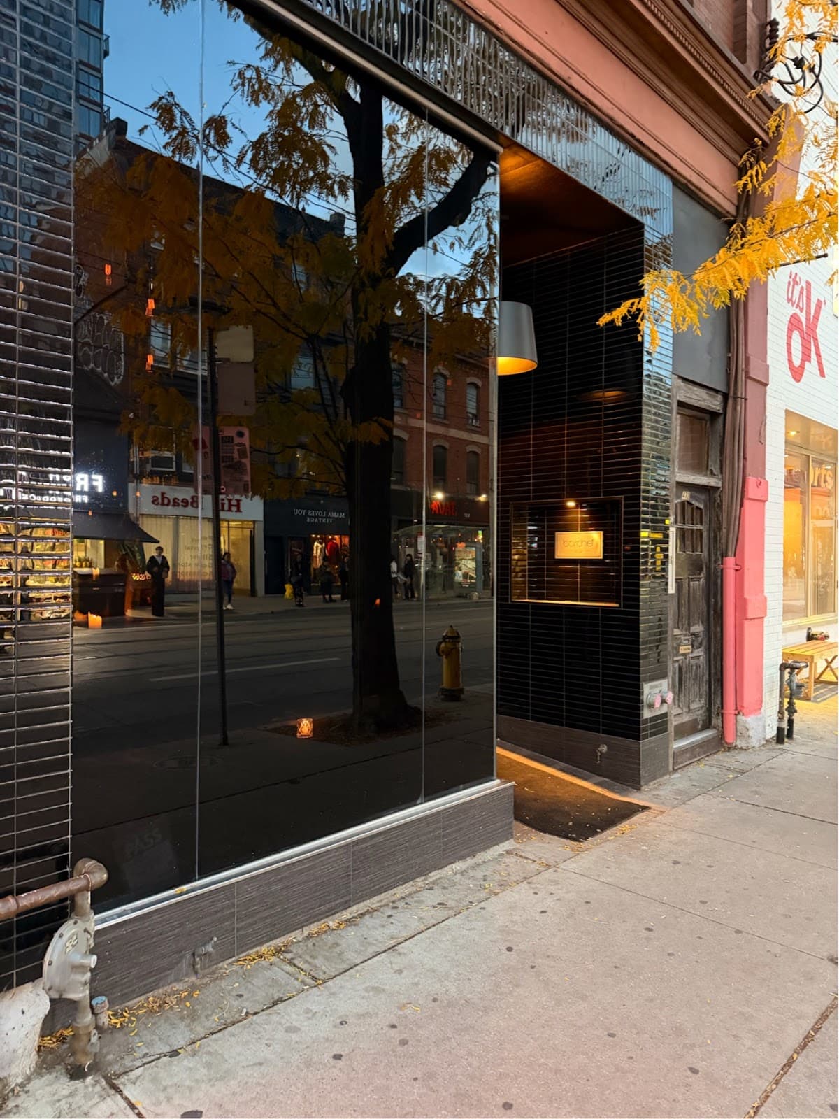 Exterior view of a cocktail bar with reflective glass windows and city street reflections in Toronto