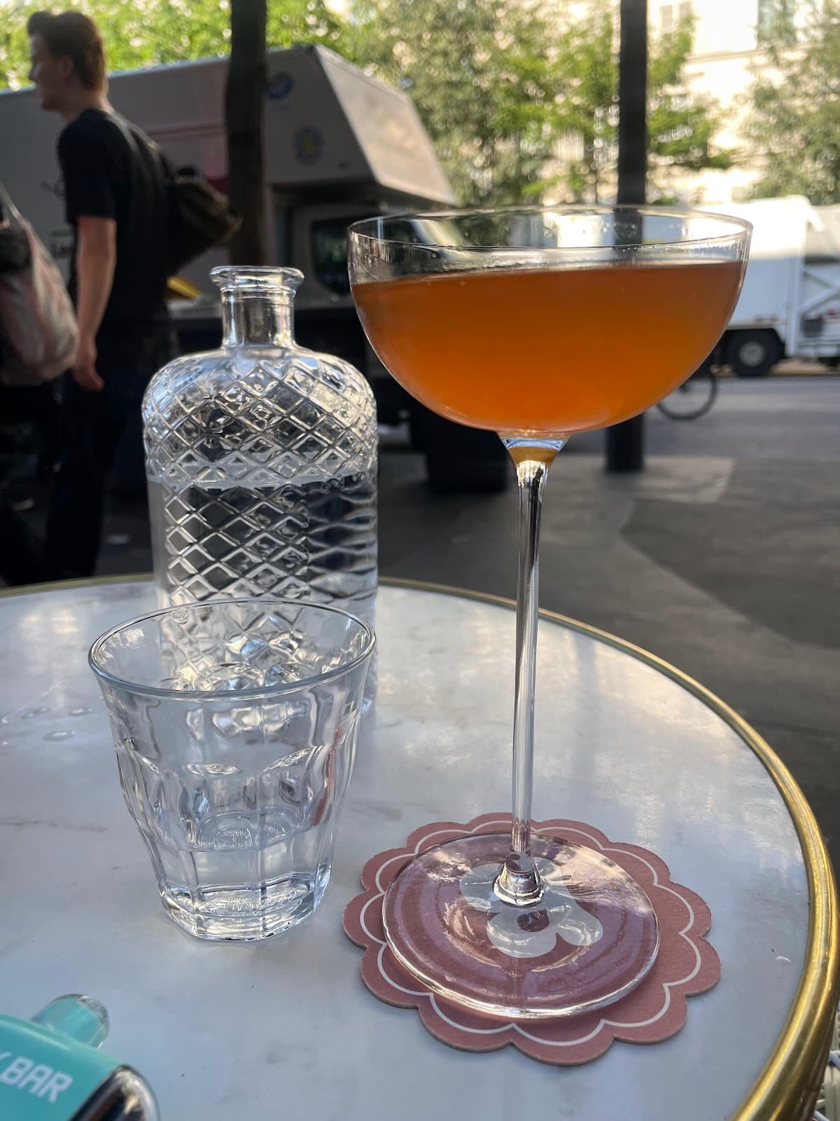 Cocktail glass on outdoor table with decanter and glass, street view in Paris