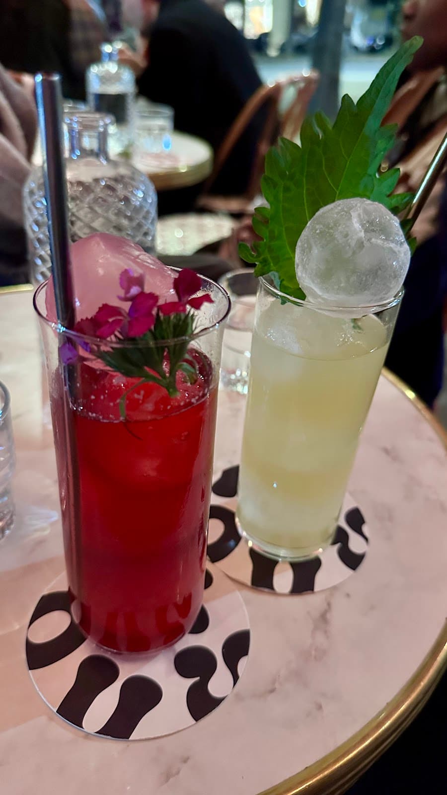 Two cocktails on a marble table with decorative coasters in Paris