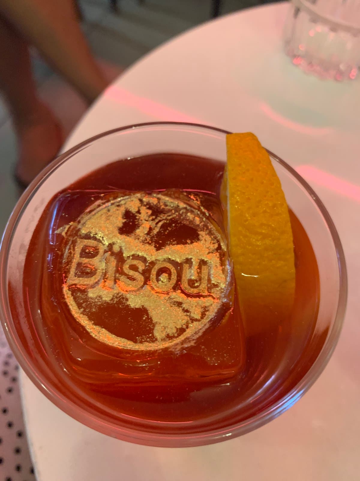 Cocktail with orange slice and branded Bisou ice cube on table in Paris