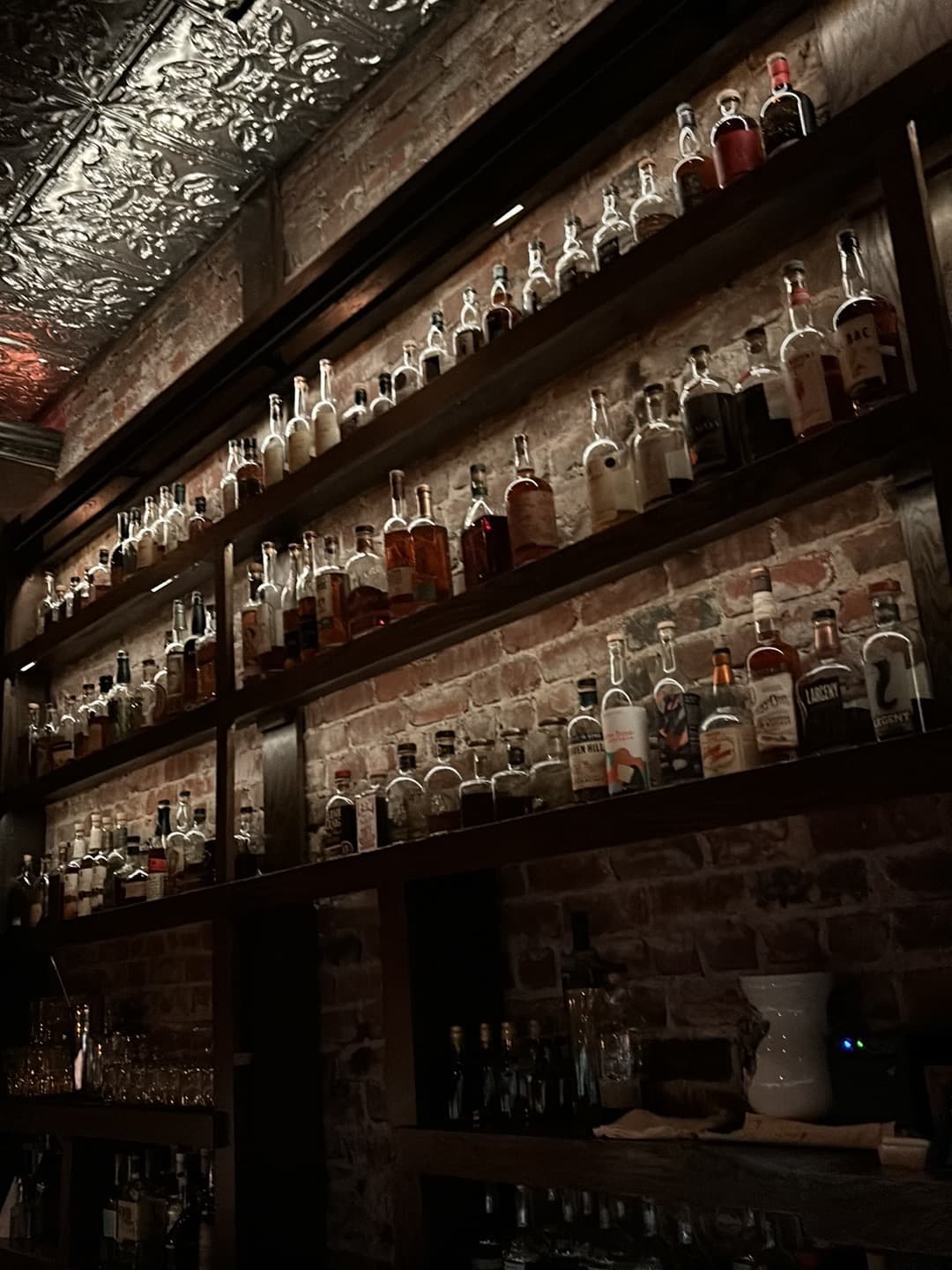 Bar shelves with bottles against a brick wall in dim lighting in San Francisco