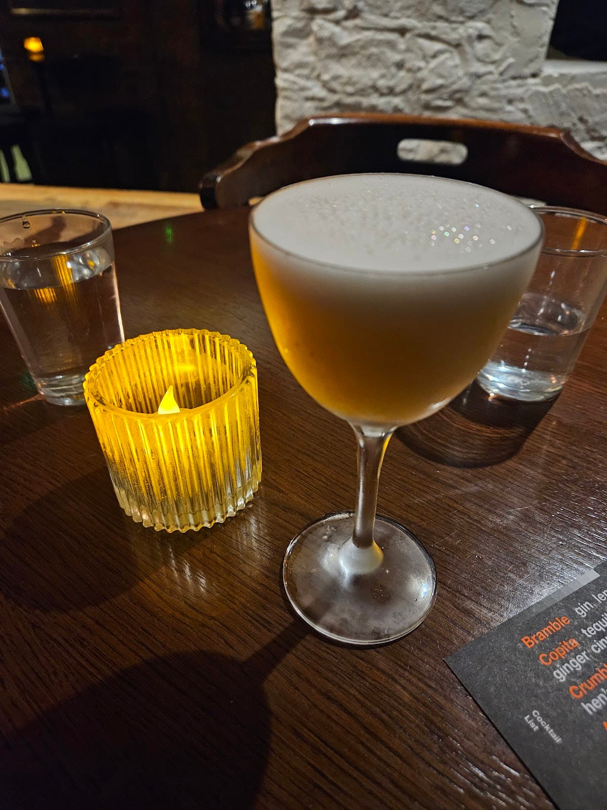 Cocktail glass on a wooden table with a candle and menu in Edinburgh