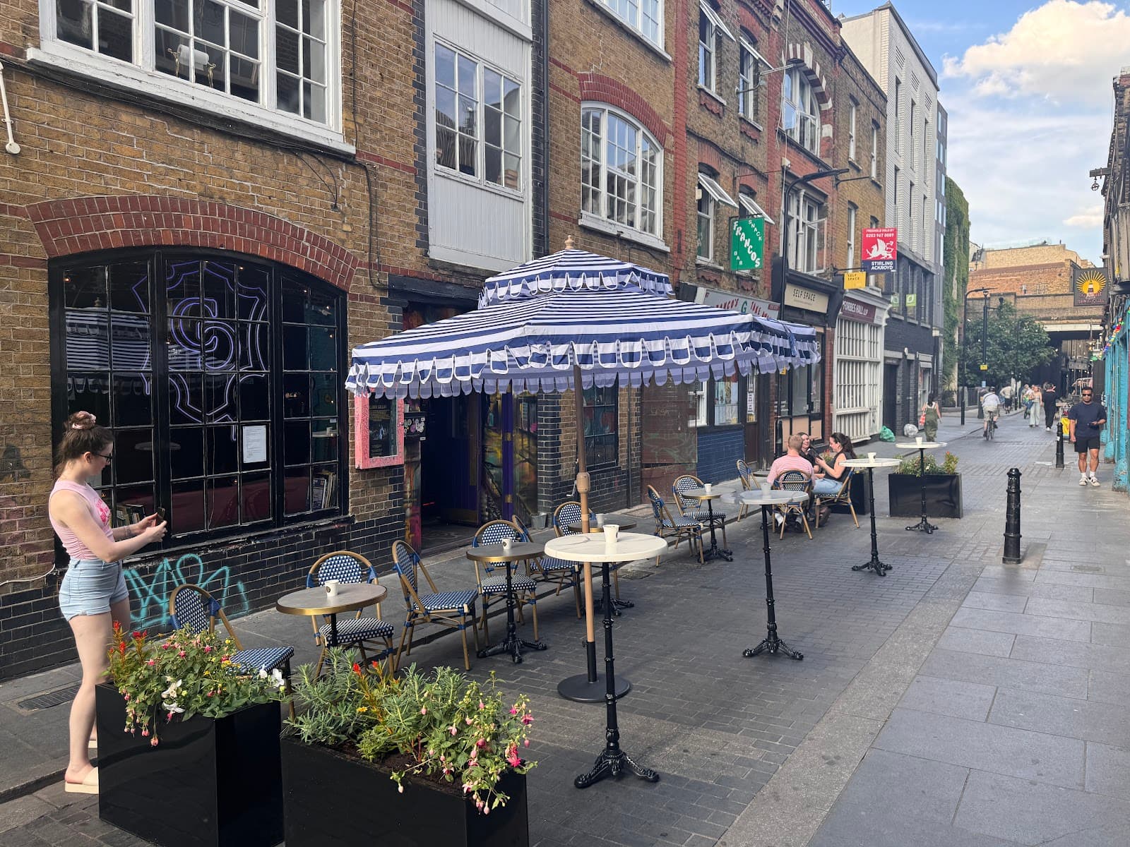 Street view of a cocktail bar with outdoor seating under striped parasols