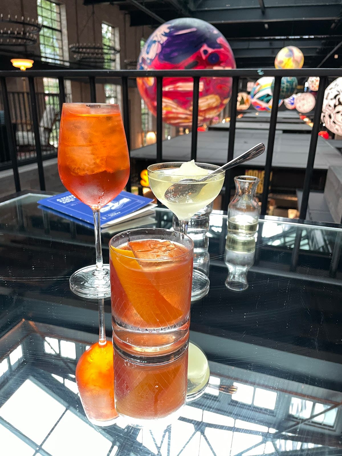 Three cocktails on a reflective table with vibrant hanging decor in Toronto