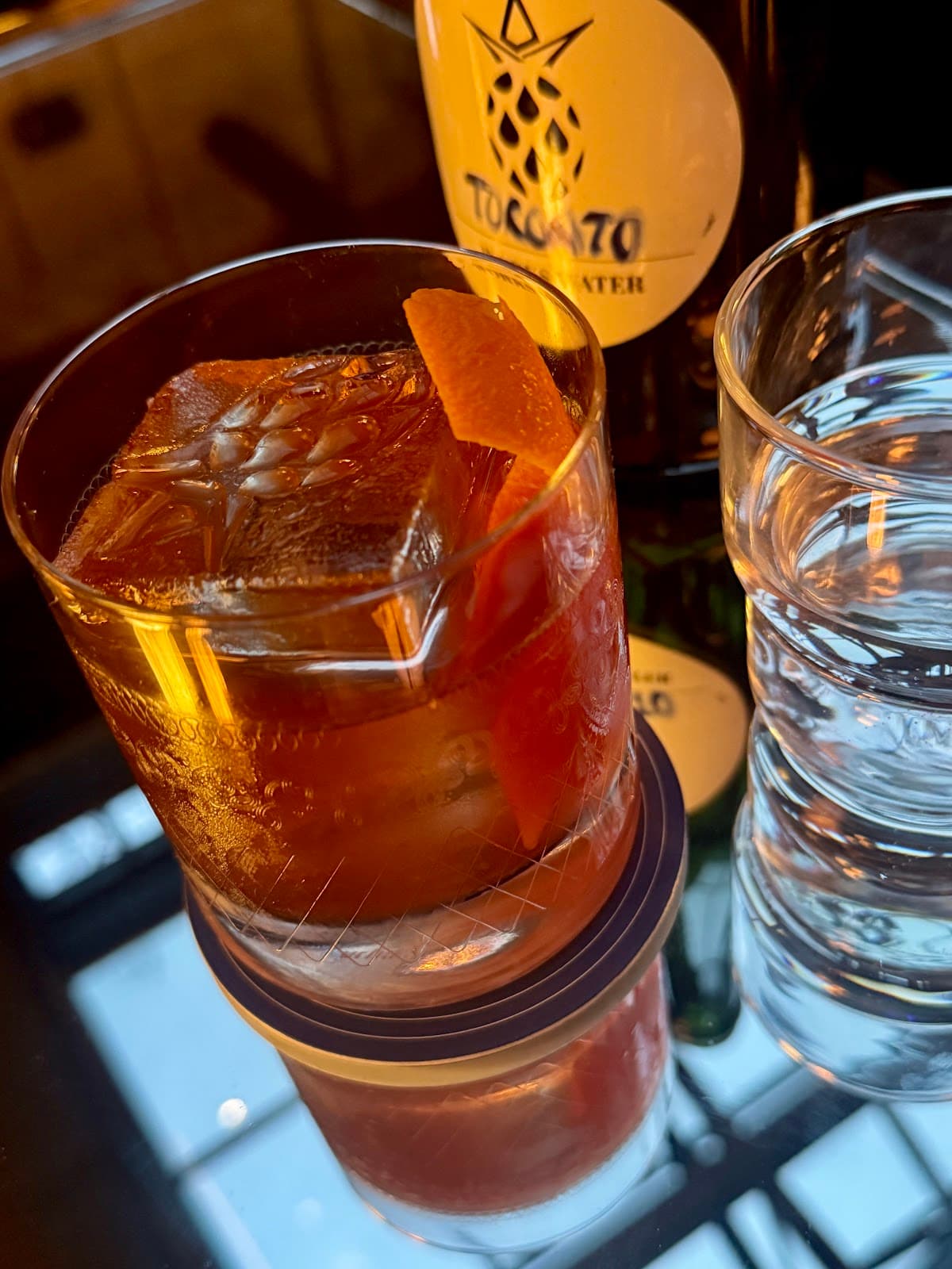 Close-up of a cocktail with an orange twist and a bottle in the background in Toronto