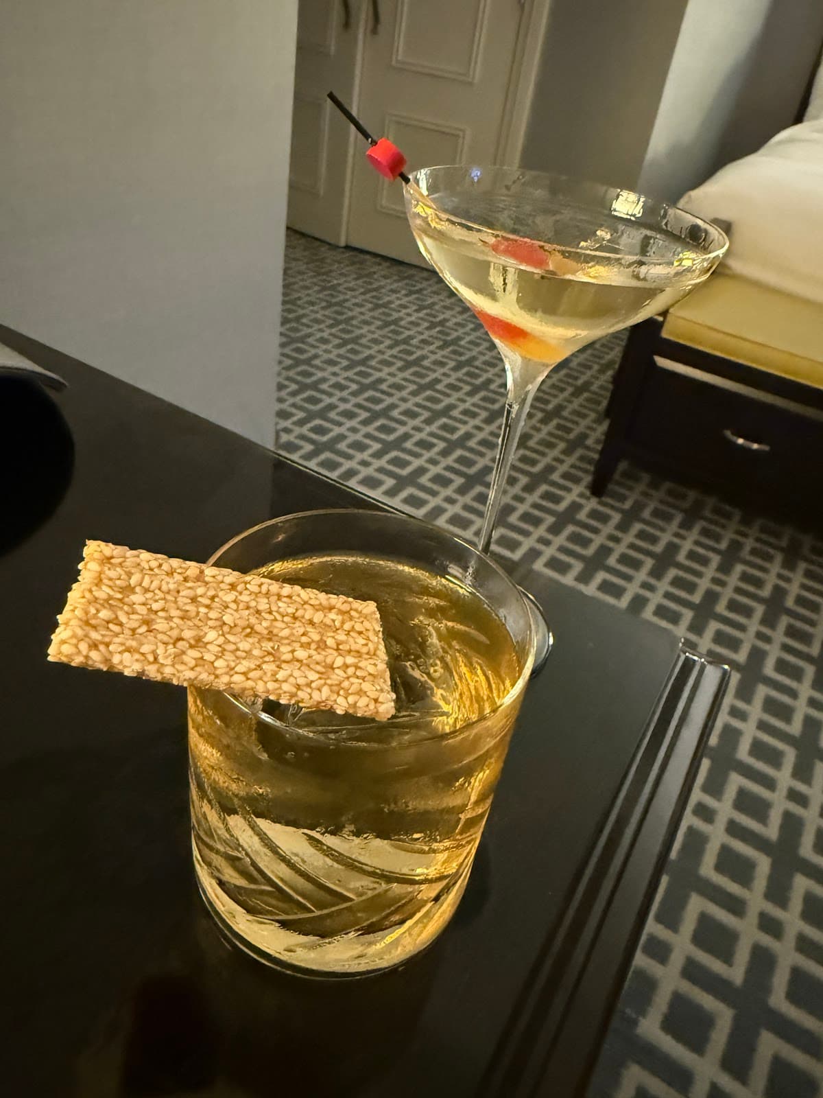 Close-up of two cocktails on a dark table surface with a sesame snack in Toronto