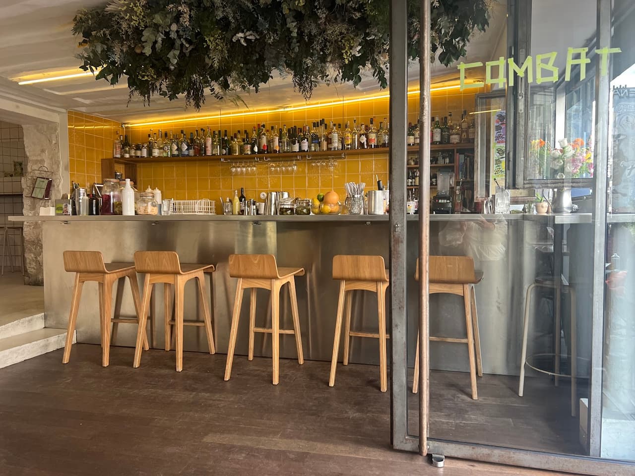 Bar counter with wooden stools and shelves of bottles at Combat in Paris