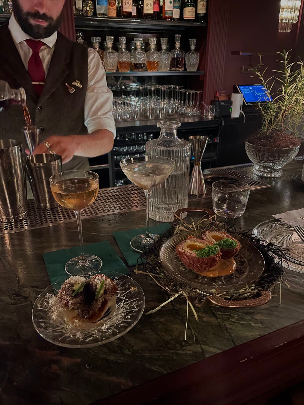 Bartender pouring a drink at a sophisticated bar with cocktails and appetizers. in Toronto