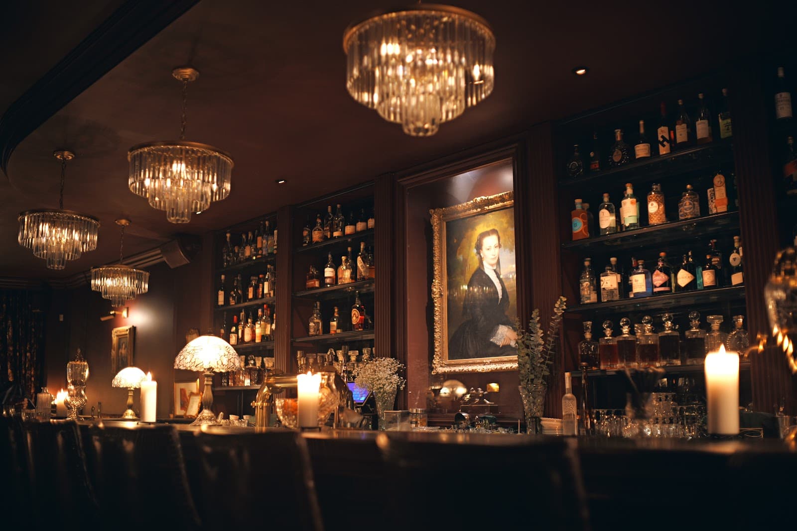 Elegant bar with chandeliers and a portrait above liquor shelves in Toronto