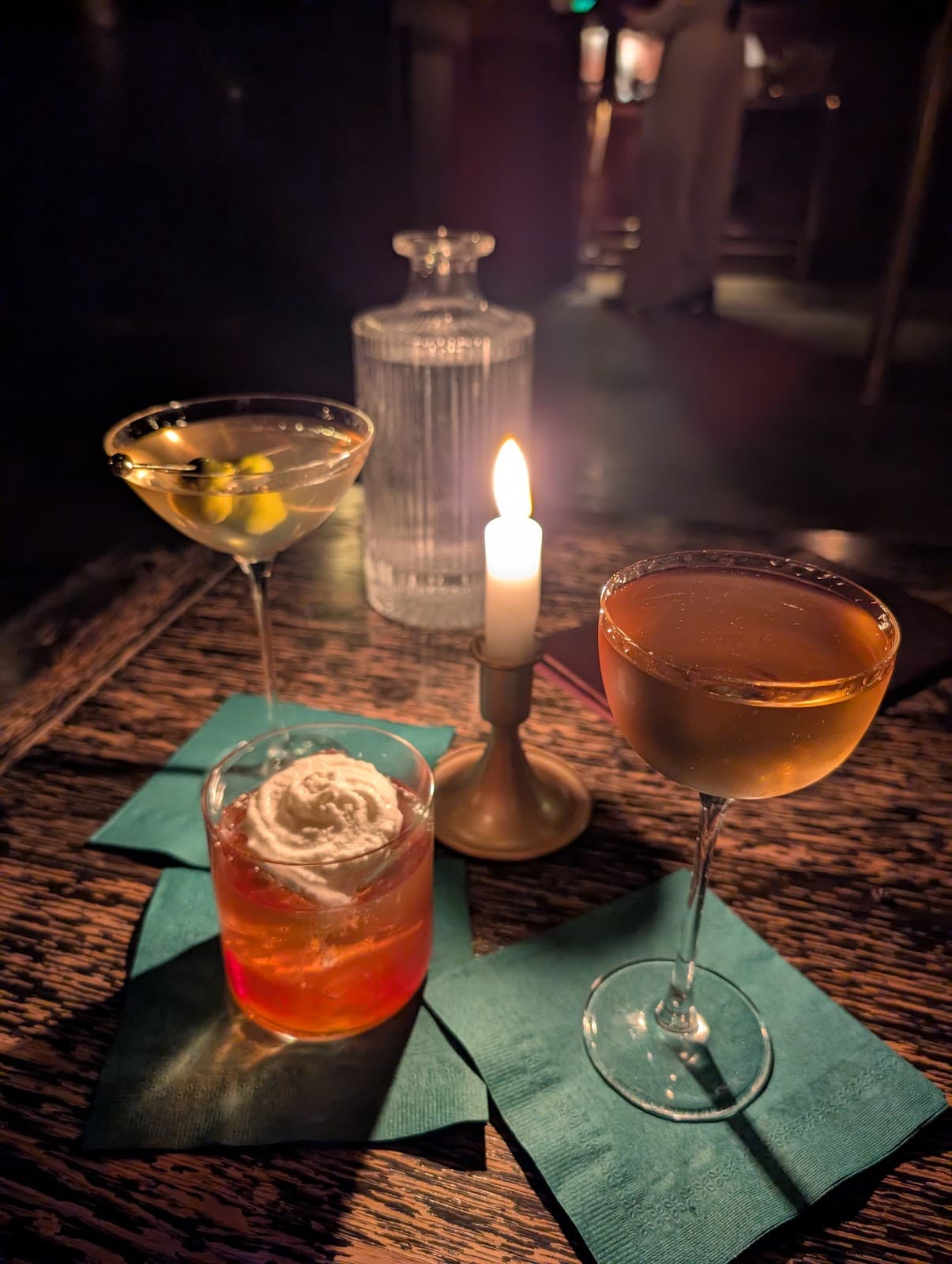 Cocktails on a wooden table with a lit candle in a dimly lit bar setting in Toronto
