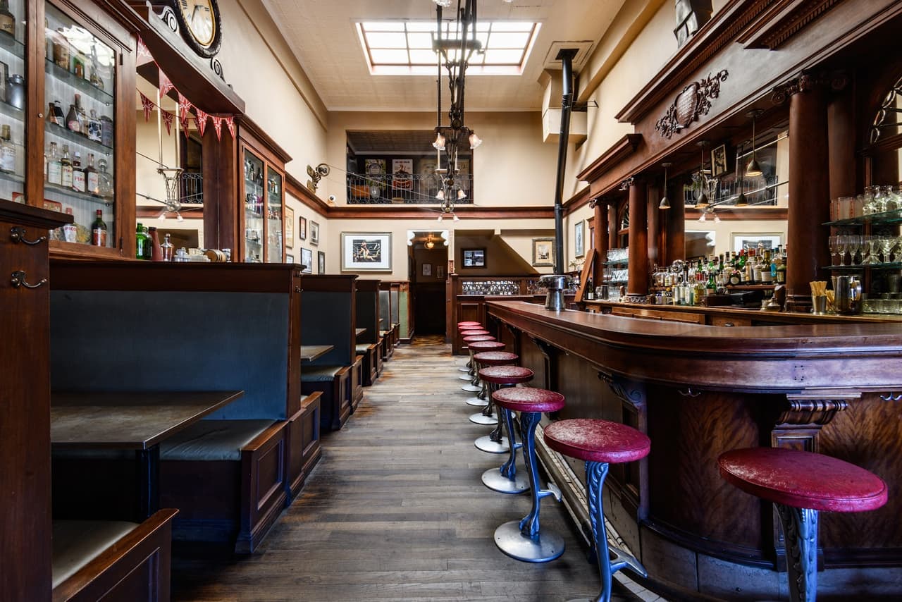Interior of a vintage-style bar with red stools and wooden booths